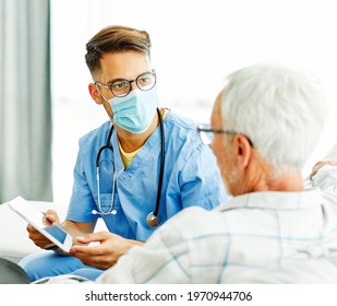 Doctor Or Nurse Caregiver Wearing A Protective Mask Helping Senior Man With A Tablet At Home Or Nursing Home