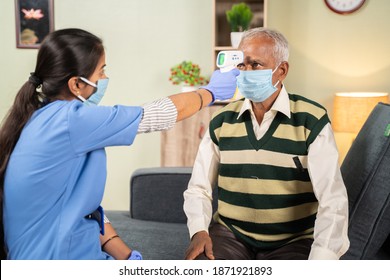 Doctor Or Nurse Checking Temperature Of Old Sick Man Using Infrared Thermometer At Hospital While Both Worn Face Mask Due To Coronavirus Covid-19 Safety Measures.