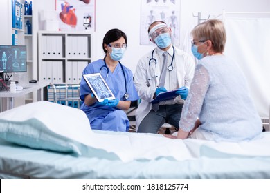 Doctor And Nurse Consulting Senior Patient During Coronavirus Outbreak In Hospital Room Wearing Face Mask. Medical Examination For Infections, Disease And Diagnosis.