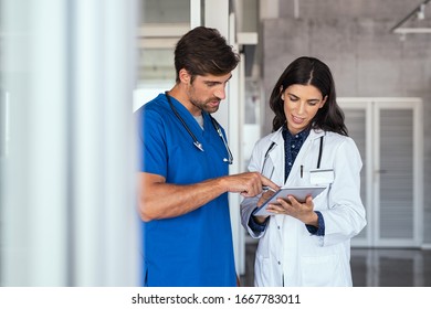 Doctor And Nurse Discussing Over A Medical Report In Hospital. Female Mature Doctor And Nurse Checking Clinical Report Of Patient Online. Healthcare Staff Standing In A Hallway Of Private Clinic. 