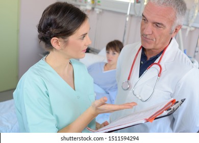 Doctor And Nurse In Discussion At Patient's Bedside