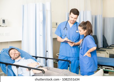 Doctor And Nurse Doing Rounds In A Hospital And Visiting A Patient, Updating Patient's Medical Report.