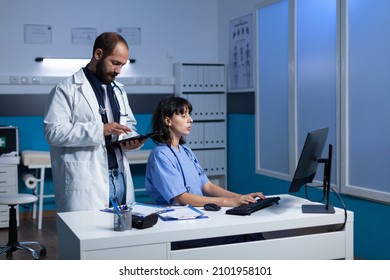 Doctor And Nurse Doing Teamwork For Medical Checkup. Medical Team Using Computer And Tablet For Healthcare System, Working Late At Night. Medic And Assistant Looking At Monitor.