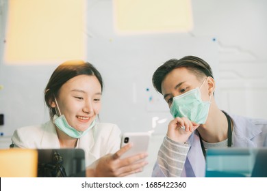 Doctor And Nurse Having Conversation During Break Lunch Time Lookign At Smartphone Inside Hospital Room.