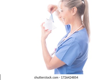 Doctor, Nurse Or  Healthcare Worker Putting On Respirator N95 Face Mask.  She Is Wearing Blue Scrubs And  Stethoscope Hangs Around Her Neck. COVID-19  Influenza Pandemic Or Other Infectious Outbreak