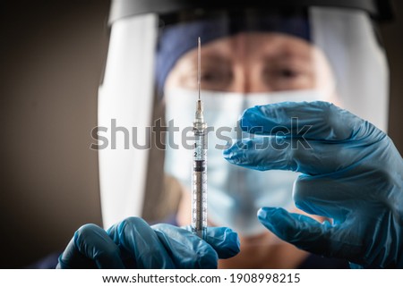 Doctor or Nurse Holding Medical Syringe with Needle AGainst Dark Background.