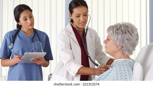 Doctor And Nurse Listening To Elderly Woman Patient's Heart And 