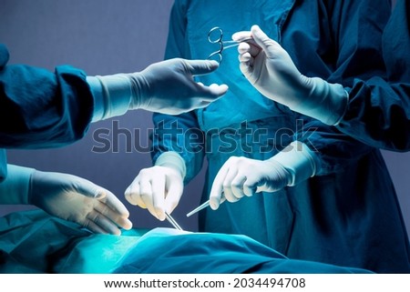 doctor and nurse medical team are performing surgical operation at emergency room in hospital. assistant hands out scissor and instruments to surgeons during operation.