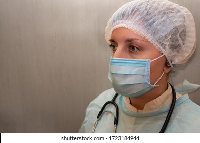 Doctor Or Nurse In Medical Uniform Mask Cap And With Stethoscope. Portrait Of White Woman Not Looking Into The Camera In Half Face Position On Light Textured Background With Copy Space