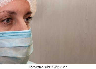 Doctor Or Nurse In Medical Uniform Mask And Cap. Close-up Portrait Of White Woman Not Looking Into The Camera In Half Face Position On Light Textured Background With Copy Space