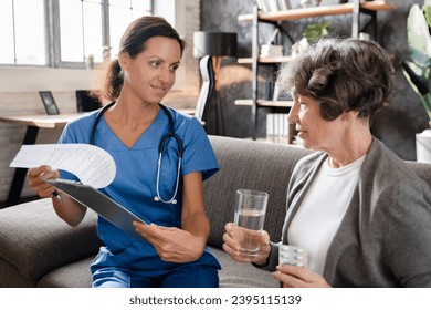 Doctor nurse medical worker explaining treatment, showing test results, prescribing medicines while elderly patient grandmother drinking water taking pills at home - Shutterstock ID 2395115139