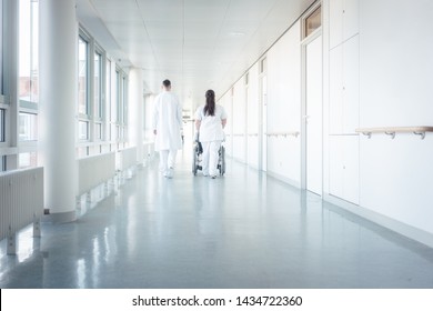 Doctor, nurse, and patient in wheelchair walking on hospital corridor