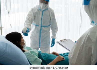 Doctor And Nurse In Personal Pretective Equipment Or Ppe Treating The Asian Woman Patient With Covid-19 Or Coronavirus Infection In The Isolation Unit In The Hospital During Pandemic. Medical Concept