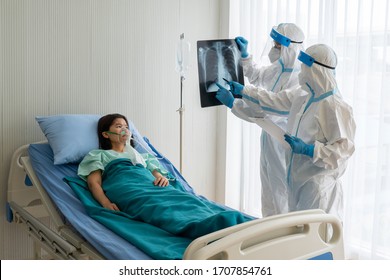 Doctor And Nurse In Personal Protective Equipment Or Ppe Looking At Chest Xray Of The Asian Woman Patient With Covid-19 Or Coronavirus Infection In The Isolation Unit In The Hospital. Medical Concept