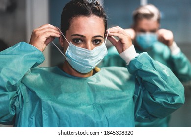 Doctor And Nurse Preparing To Work In Hospital For Surgical Operation During Coronavirus Pandemic Outbreak - Medical Workers Getting Dressed Inside Clinic - Focus On Woman Face 