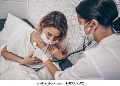 Doctor nurse in protective face mask listening to breath with a stethoscope suspecting Coronavirus (COVID-19). First symptoms concept. Woman sick of flu viral infection in home isolation quarantine - Shutterstock ID 1683387502
