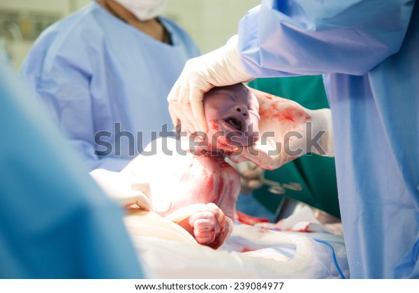 Doctor and nurse are  pulling a new born baby\
from mom\'s abdomen
