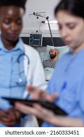 Doctor And Nurse Reading Digital Test Results On Tablet For Man With Low Spo2 Saturation Waiting Diagnosis. Patient With Illness Waiting While Medical Caregivers Looking At Imaging Device.