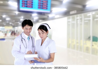 Doctor And Nurse Reviewing Medical Chart,  In Hospital Hallway