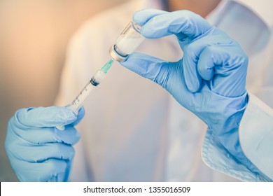 Doctor, Nurse Or Scientist Holding Flu, Hpv, Rabies, Mumps, Measles, Polio, Or Diphtheria Vaccine Bottle With Syringe And Needle Prepare For Immunization 