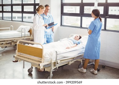 Doctor and a nurse stand around a patients bed as they are examining him in hospital - Powered by Shutterstock