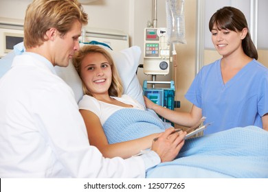 Doctor With Nurse Talking To Teenage Female Patient In Bed