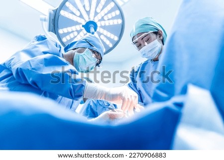 Doctor and nurse team in blue uniform did surgery inside operating room in hospital.Asian surgeon did orthopedic or cosmetic surgery.Surgical treatment in theater.Medical device used in hospital.