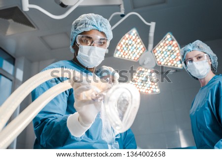doctor and nurse in uniforms and medical caps holding mask in operating room