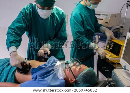 Doctor and nurse using defibrillator to pump at chest of unconscious with low heart rate patient to save life while doing medical surgery inside of operating room. Emergency aid, CPR.