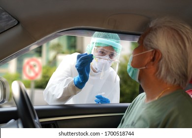 Doctor Or Nurse Wearing PPE, N95 Mask, Face Shield  And Personal Protective Gown Standing Beside The Car/road Screening For Covid-19 Virus, Nasal Swab Test  