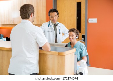 Doctor And Nurse Working At Reception Desk While Man Standing In Hospital