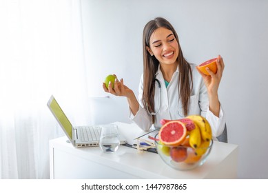 Doctor Or Nutritionist Hold An Apple. Good Medical Healthcare Nutrition Concept. An Apple A Day Keeps The Doctor Away. Smiling Female Nutritionist Holding A Green Apple And Showing Healthy Fruits
