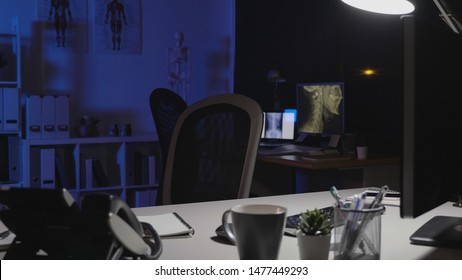 Doctor Office Table Desk And Black Chair Telephone. Dark Indoor Interior Of Working Medical Staff With Bone X-ray On Computer Screen. Empty Room In Midnight In Clinic Office Hospital At Night.