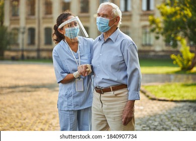 Doctor And Old Patient Wearing Masks And Standing Outdoors While Walking In The Hospital Yard