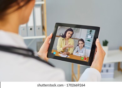 Doctor Online. A Female Doctor Therapist Is Looking At The Screen Of A Tablet While The Family Is Listening To The Mother And Her Daughter.