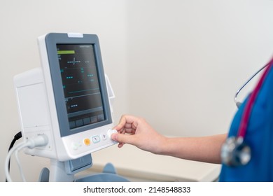 Doctor Operating Vital Sign Monitor In Patient Room Of Modern Hospital.