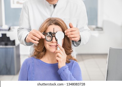 Doctor Ophthalmologist Examining Eyesight Of Patient With Special Medical Device. Eye Specialist Holding Test Glasses, Woman Wearing In Ophtalmology Equipment.