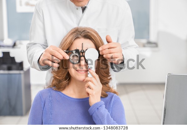 Doctor ophthalmologist examining\
eyesight of patient with special medical device. Eye specialist\
holding test glasses, woman wearing in ophtalmology\
equipment.