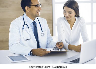 Doctor and patient discussing medical exam results while sitting at the desk in clinic. Male physician using clipboard for filling up medication history record of young woman. Data in medicine