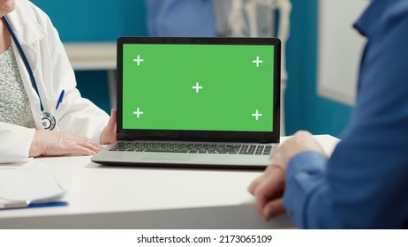 Doctor And Patient Looking At Laptop With Greenscreen Display At Medical Appointment. Mockup Copyspace Background With Blank Chroma Key And Isolated Template On Computer. Close Up.