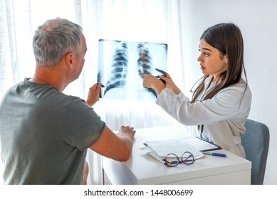 Doctor And Patient Looking At Xray In Medical Office. Doctor Shows The Patient Chest X-ray. Doctor And Patient Looking At Chest X-ray Together. Doctor Talking With Female Patient In Doctors Office.

