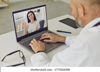 Doctor and patient online. Girl patient says consults using laptop webcam with senior man doctor at virtual clinic.