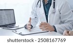 Doctor and a patient. The physician, wearing a white medical coat over a green shirt, is gesturing with his hands during a consultation in the clinic. Medicine