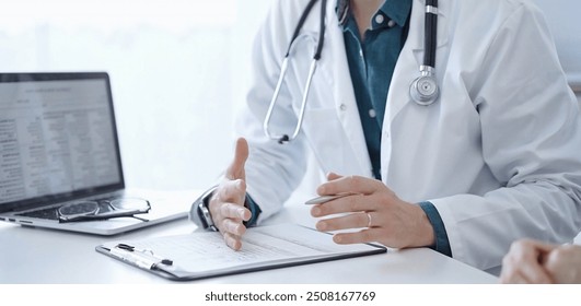 Doctor and a patient. The physician, wearing a white medical coat over a green shirt, is gesturing with his hands during a consultation in the clinic. Medicine - Powered by Shutterstock