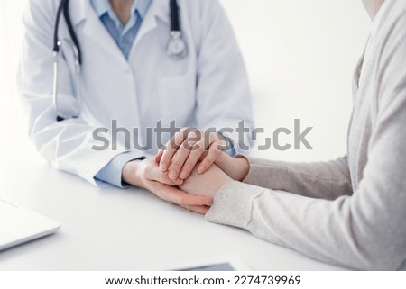 Doctor and patient sitting at the table in clinic office. The focus is on female physician's hands reassuring woman, only hands close up. Medicine concept.