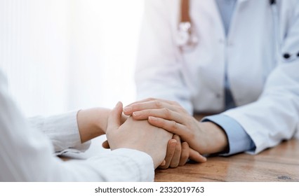 Doctor and patient sitting at the wooden table in clinic. Female physician's hands reassuring woman. Medicine concept - Shutterstock ID 2332019763