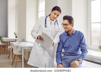 Doctor and patient talking during a medical check up at the hospital. Young woman in a white coat shows good analysis results to a happy young man sitting on the medical couch in the examination room - Powered by Shutterstock