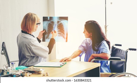 Doctor and patient who sitting in wheelchair with saline drip looking at x-ray film together.Professional caucasian doctor with stethoscope consult stress patient. Medical and healthcare concept.