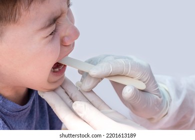 Doctor Pediatrician Checking Boy Kid Throat With Wooden Spatula.spatula On Tongue,wide Open Mouth Crying Upset Sad Child.medical Assistance Hands In White Surgical Gloves.sore Throat Redness Angina