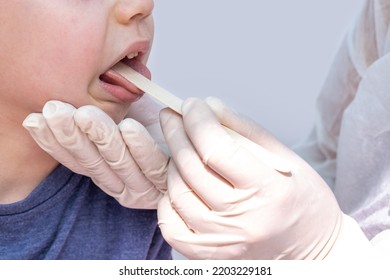 Doctor Pediatrician Checking Boy Kid Throat With Wooden Spatula.spatula On Tongue,wide Open Mouth Crying Upset Sad Child.medical Assistance Hands In White Surgical Gloves.sore Throat Redness Angina